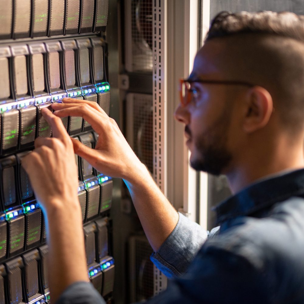 Serious busy hipster IT specialist standing by open cabinet and examining network racks while analyzing provider of server